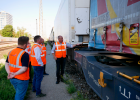 Hier sind 4 Personen mit orangenen Warnwesten vor einem Güterzug zu sehen. 