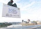 Ein großes Plakat mit der Aufschrift "30 Jahre Main-Donau-Kanal" wird mit einem Kran nach oben gezogen. Im Hintergrund der Hafen Bamberg.