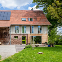 Ein umgebautes Bauernhaus mit großzügigen Fensterflächen und einem grünen Garten