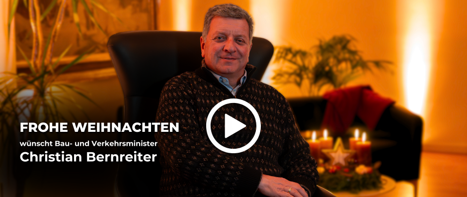 Staatsminister Christian Bernreiter sitzt in einem Sessel. Der Hintergrund ist weihnachtlich beleuchtet. Text: Frohe Weihnachten wünscht Bau- und Verkehrsminister Christian Bernreiter. Beim Klick auf das "Play"-Symbol gelangt man zum YouTube-Video mit der Weihnachtsbotschaft. - &copy; StMB