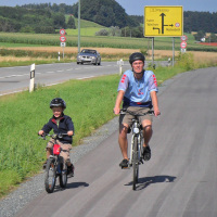 Vater und Sohn radeln auf einem Radweg an der B12